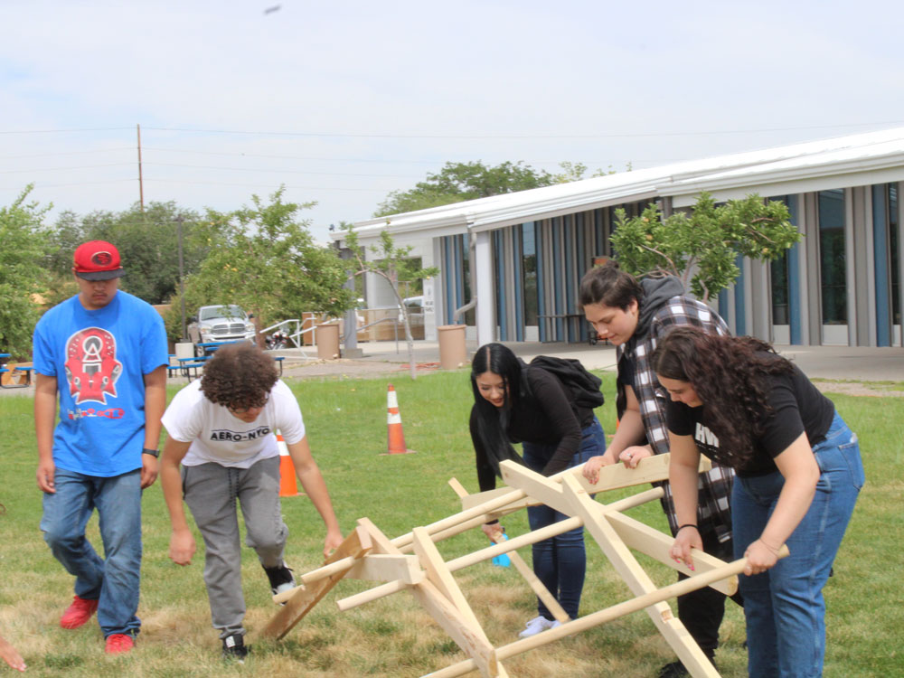 Decorative photo of students lifting a wood frame together outside.